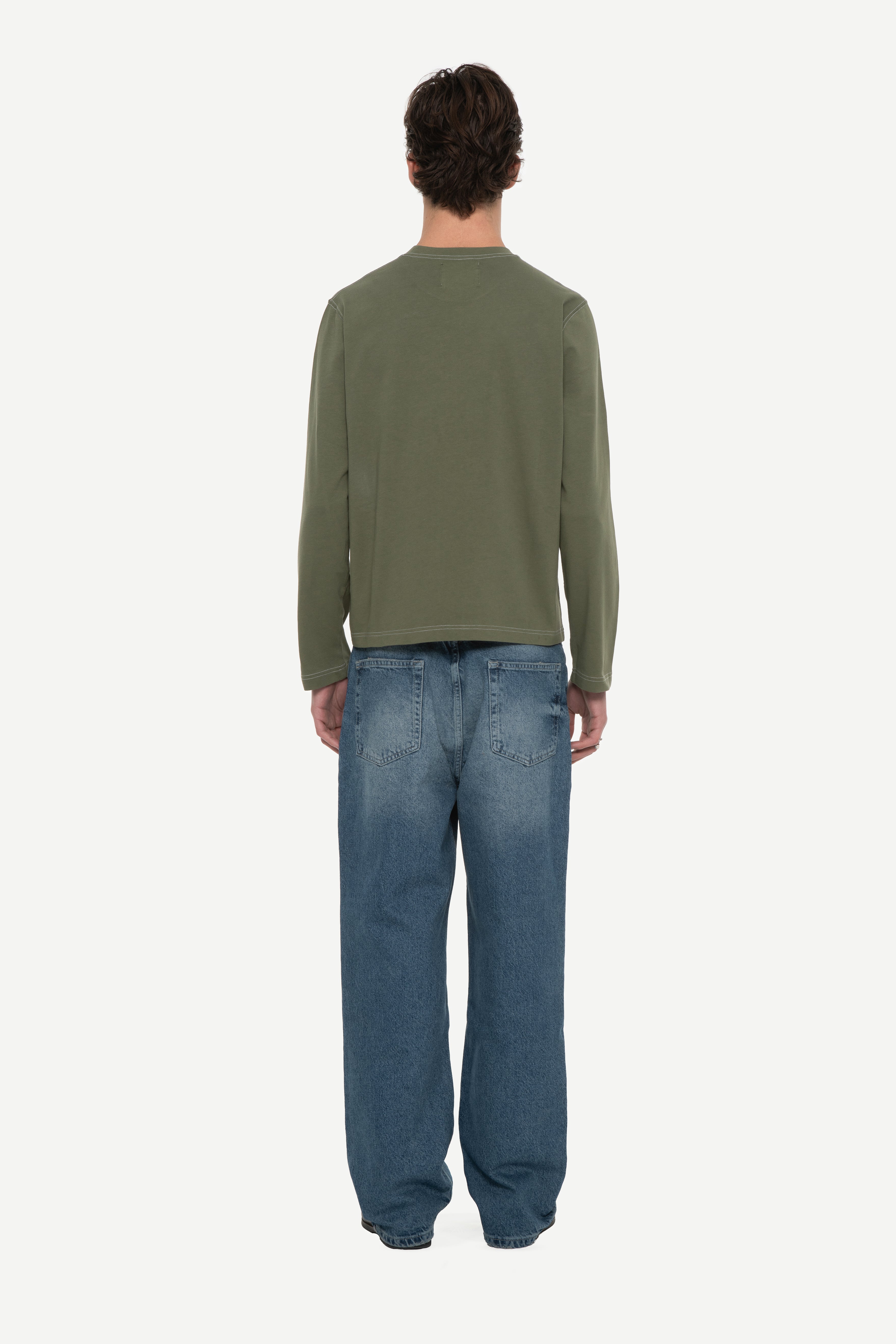 back view of man wearing a military green long sleeve tee with contrast stitching and blue jeans on a white background