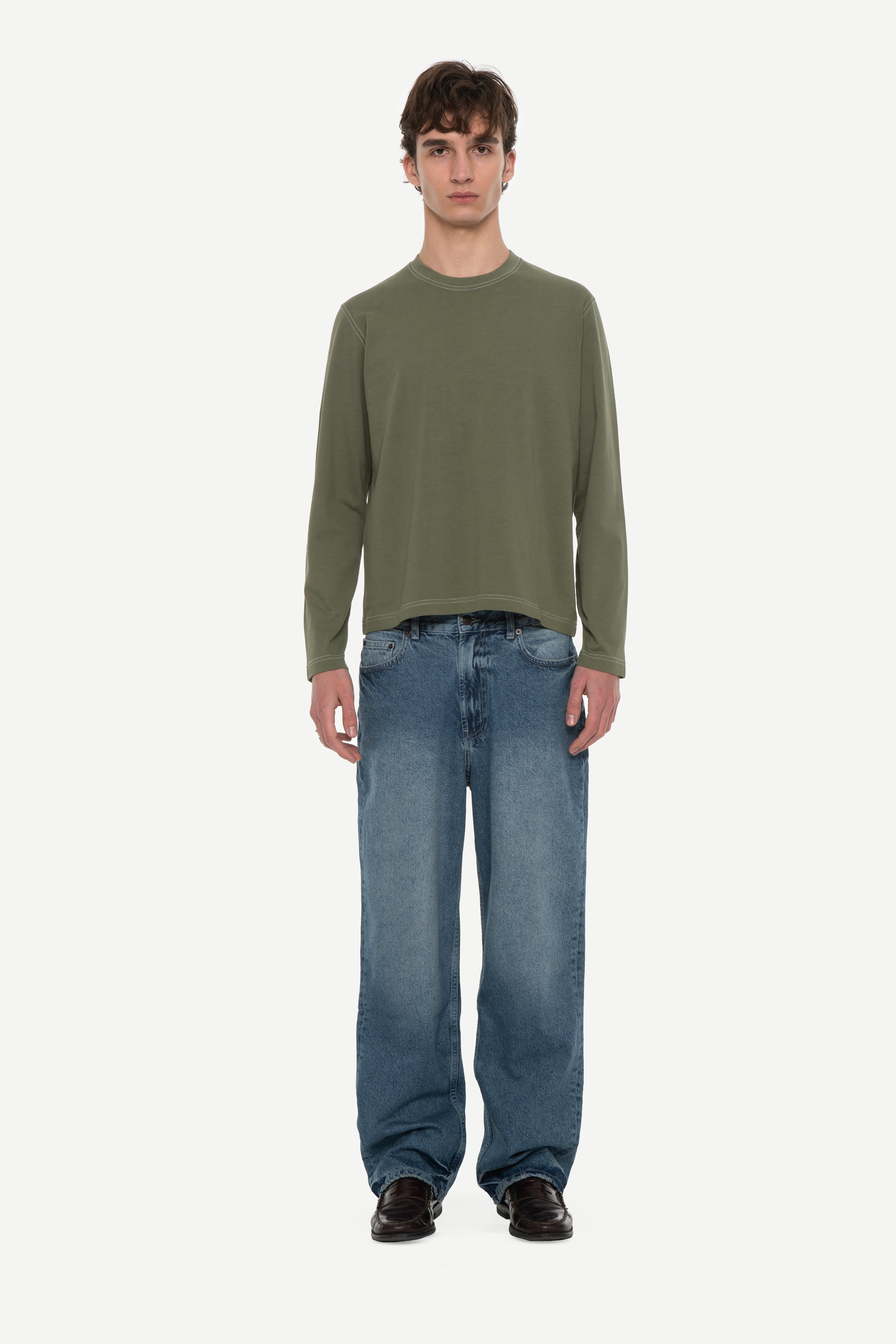 front view of man wearing a military green long sleeve tee with contrast stitching and blue jeans on a white background