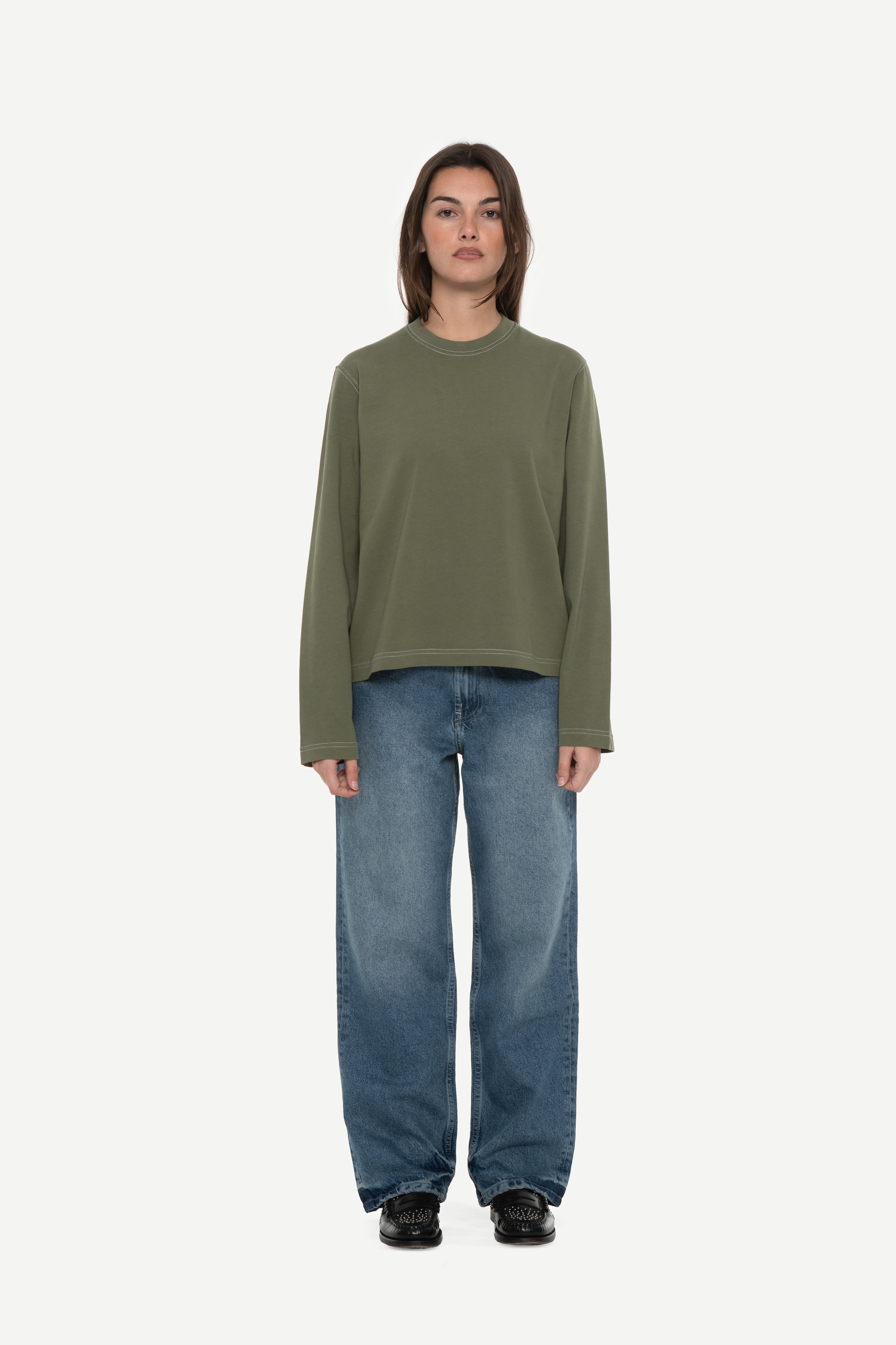 front view of woman wearing a military green long sleeve tee with contrast stitching and blue jeans on a white background
