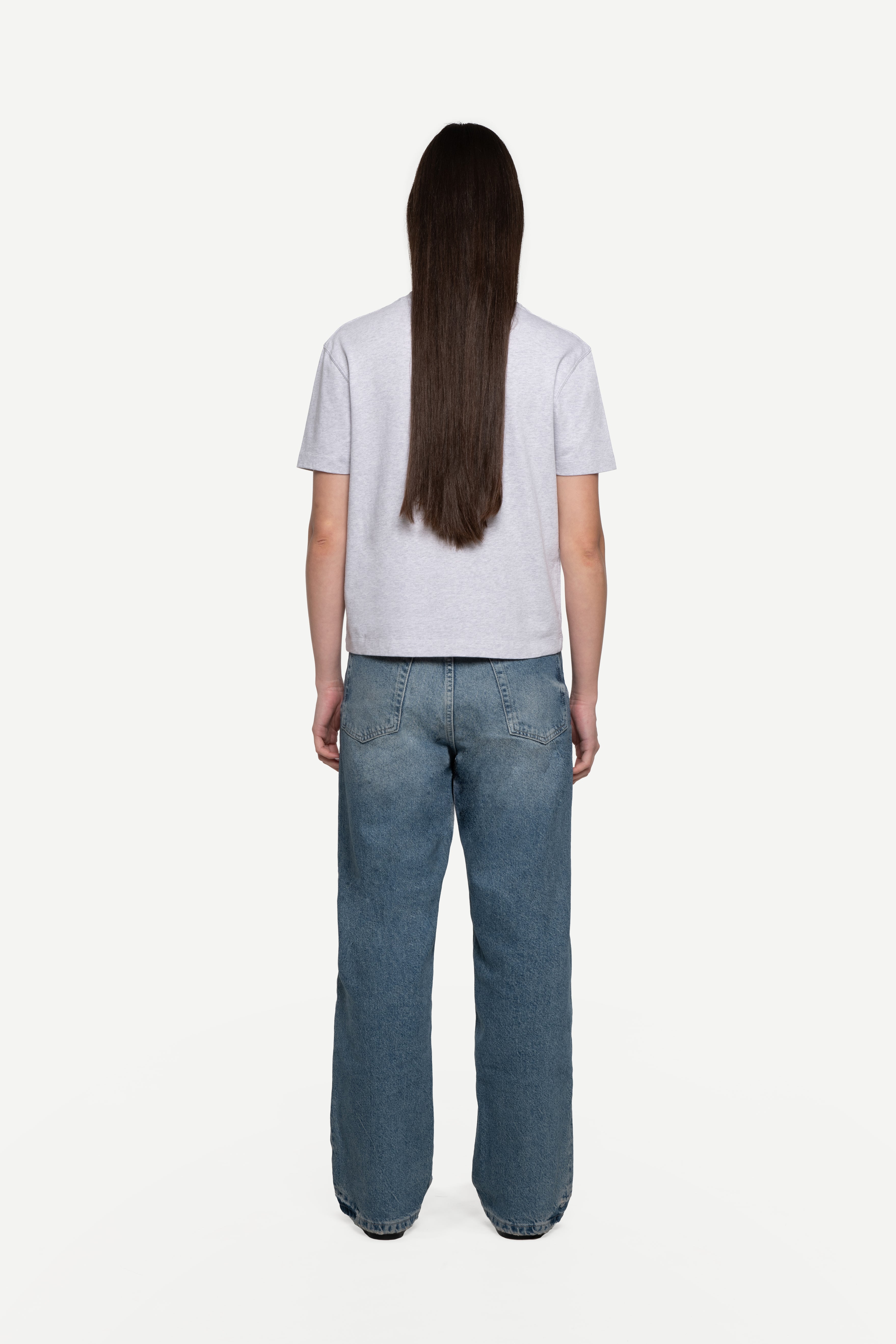 back view of woman wearing a regular fit short-sleeved grey melange t-shirt with blue jeans on a white background