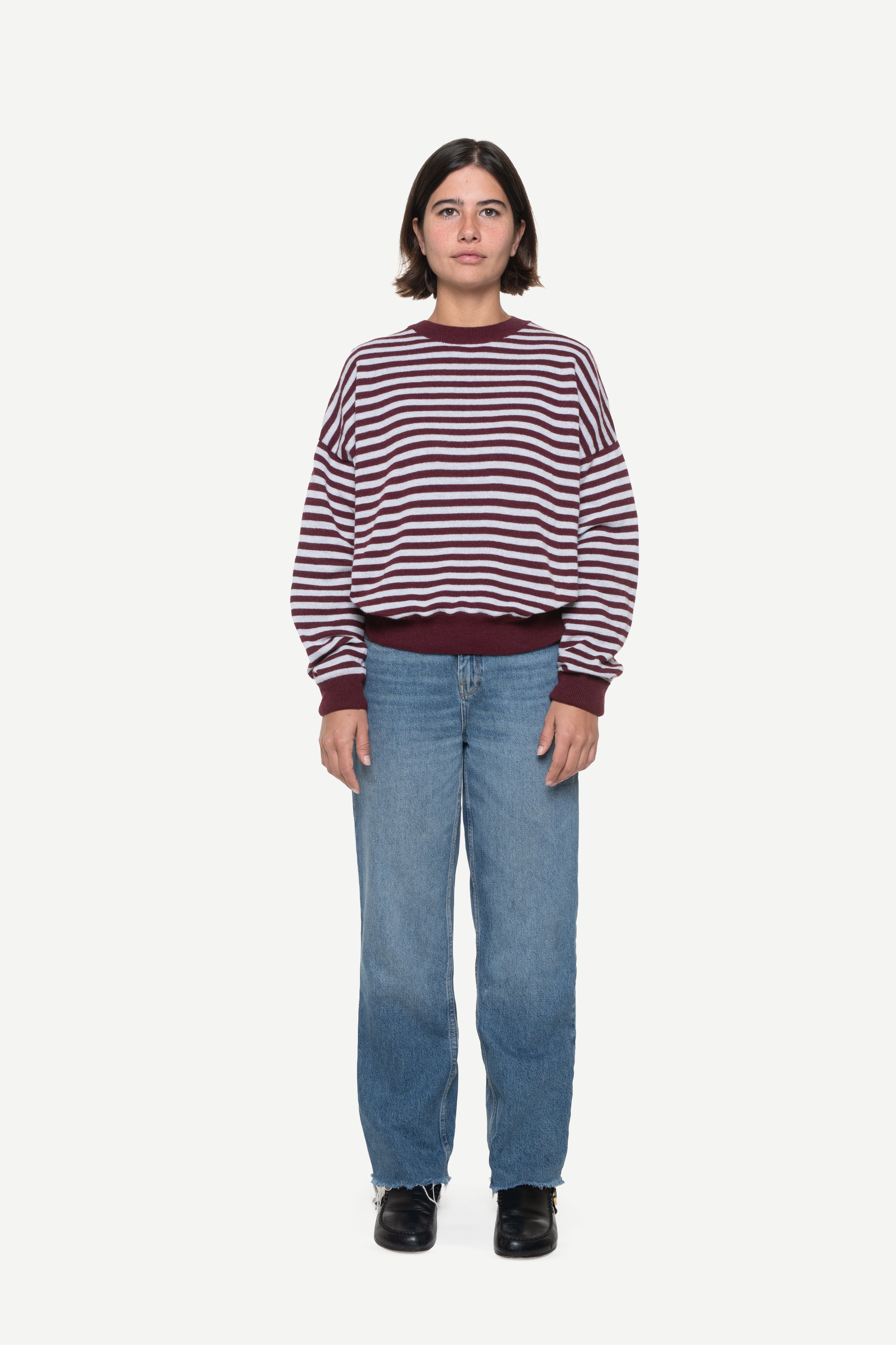 woman wearing a burgundy knit striped sweater and jeans on a white background