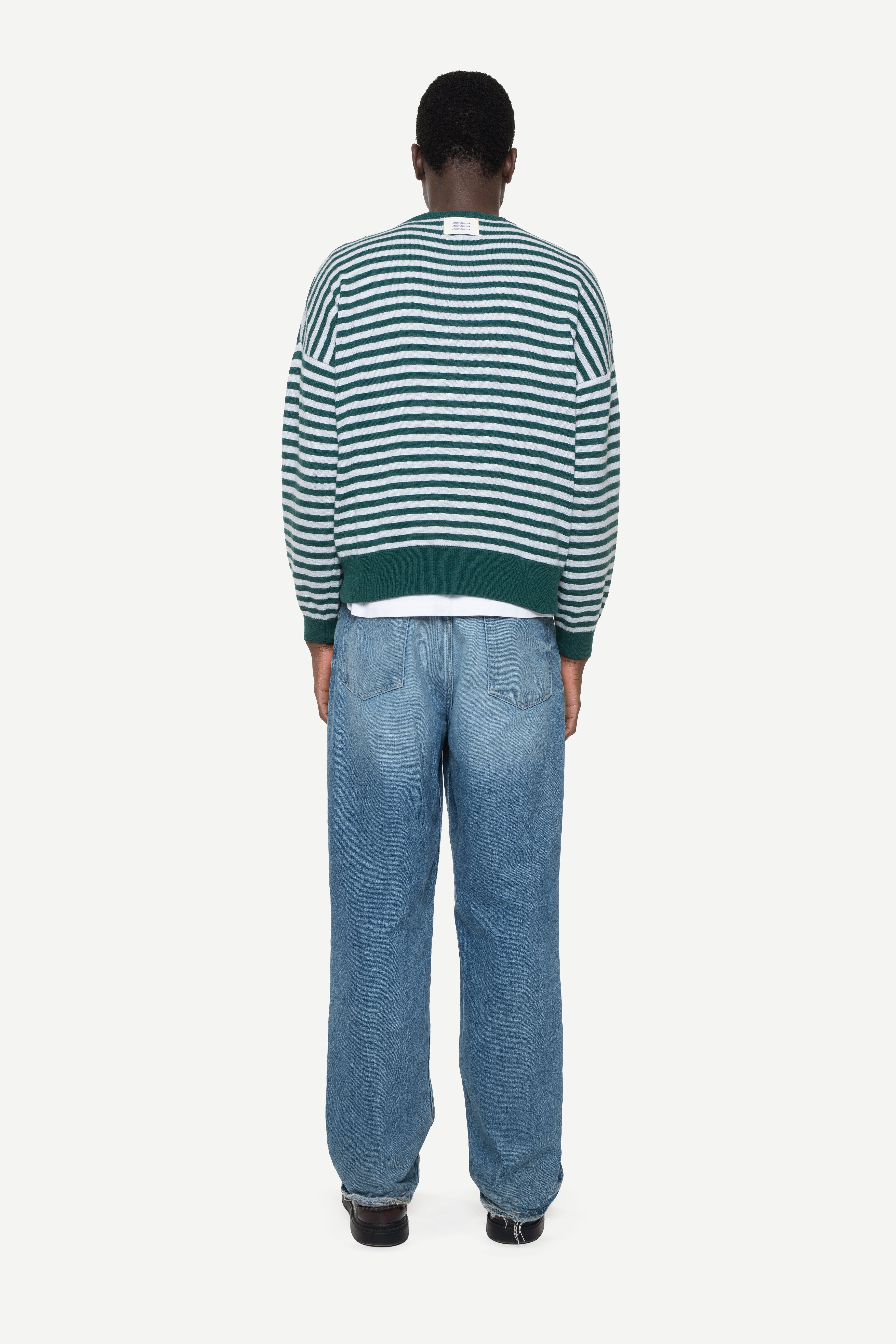 back view of a man wearing a green knit striped sweater with demossa label and jeans on a white background