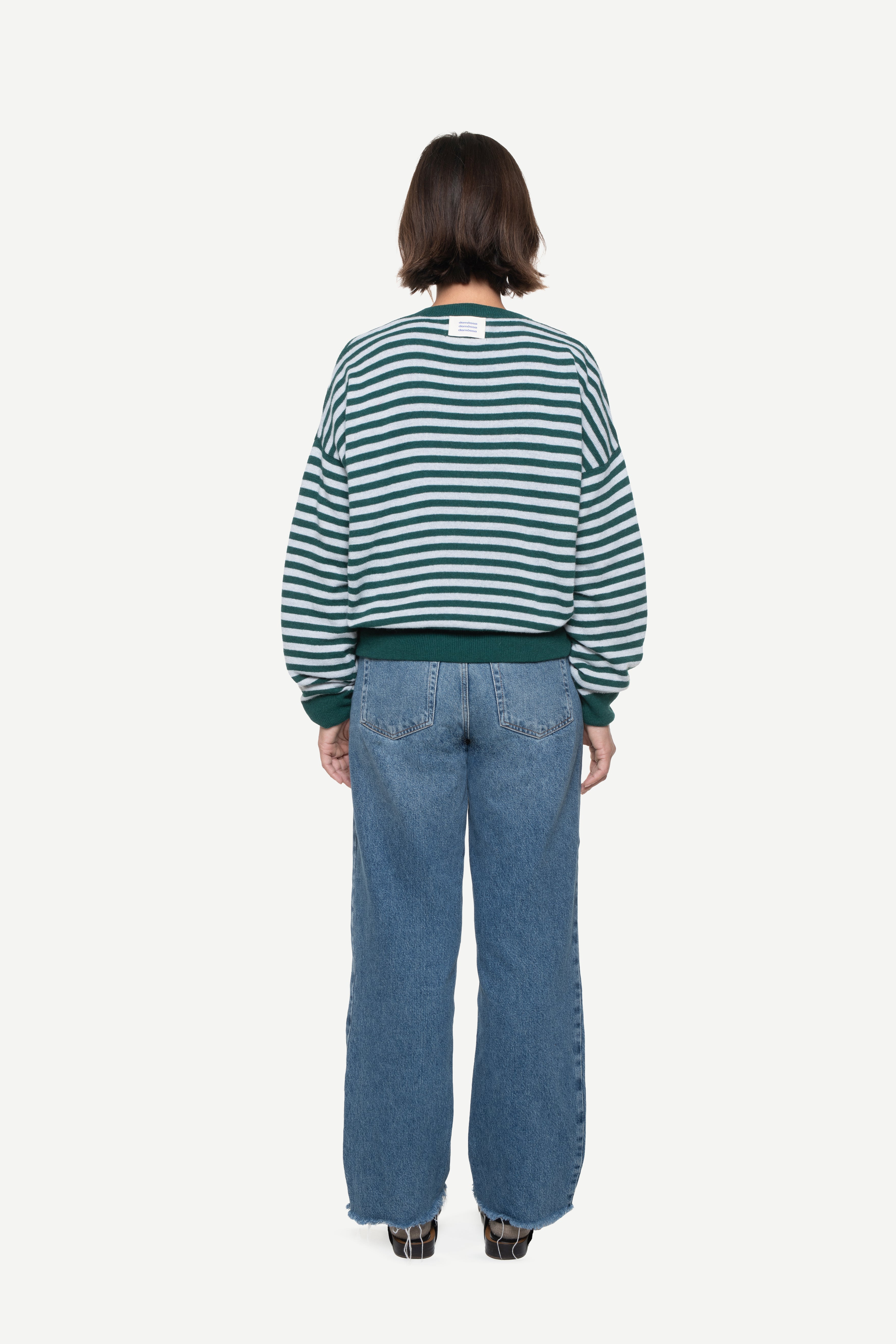 back view of a woman wearing a blue knit striped sweater with demossa label and jeans on a white background