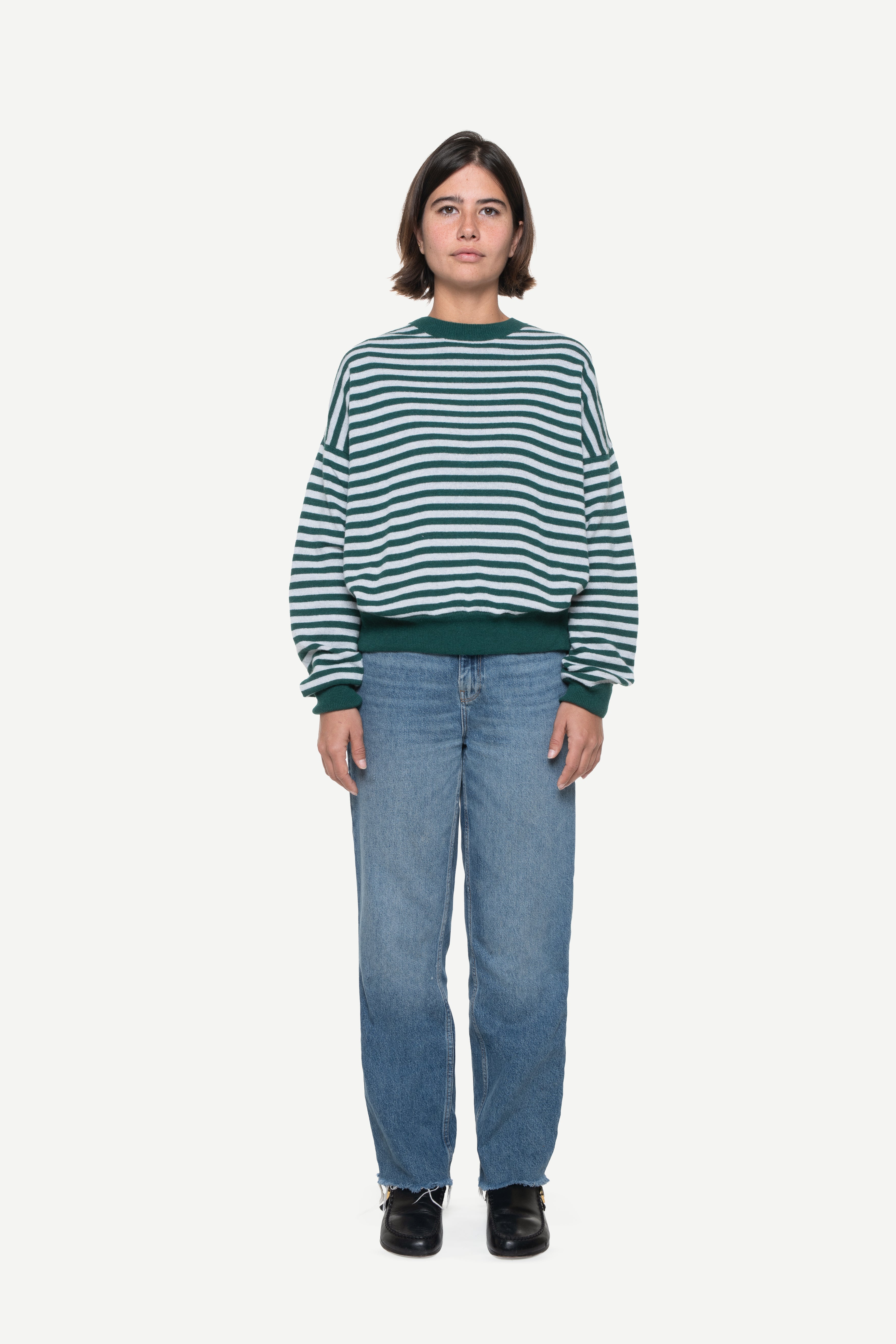 woman wearing a green knit striped sweater and jeans on a white background