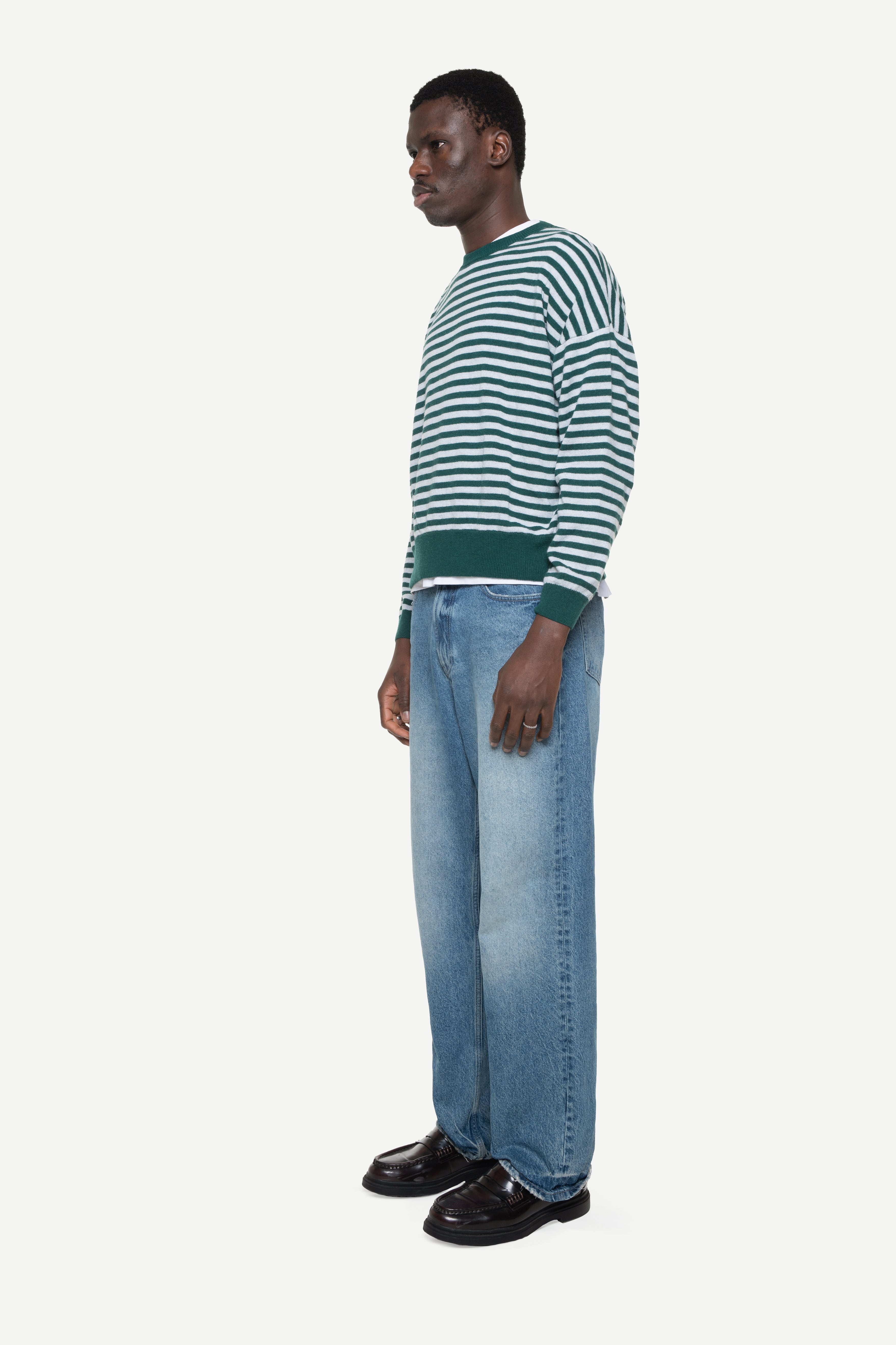 side view of a man wearing a green knit striped sweater and jeans on a white background