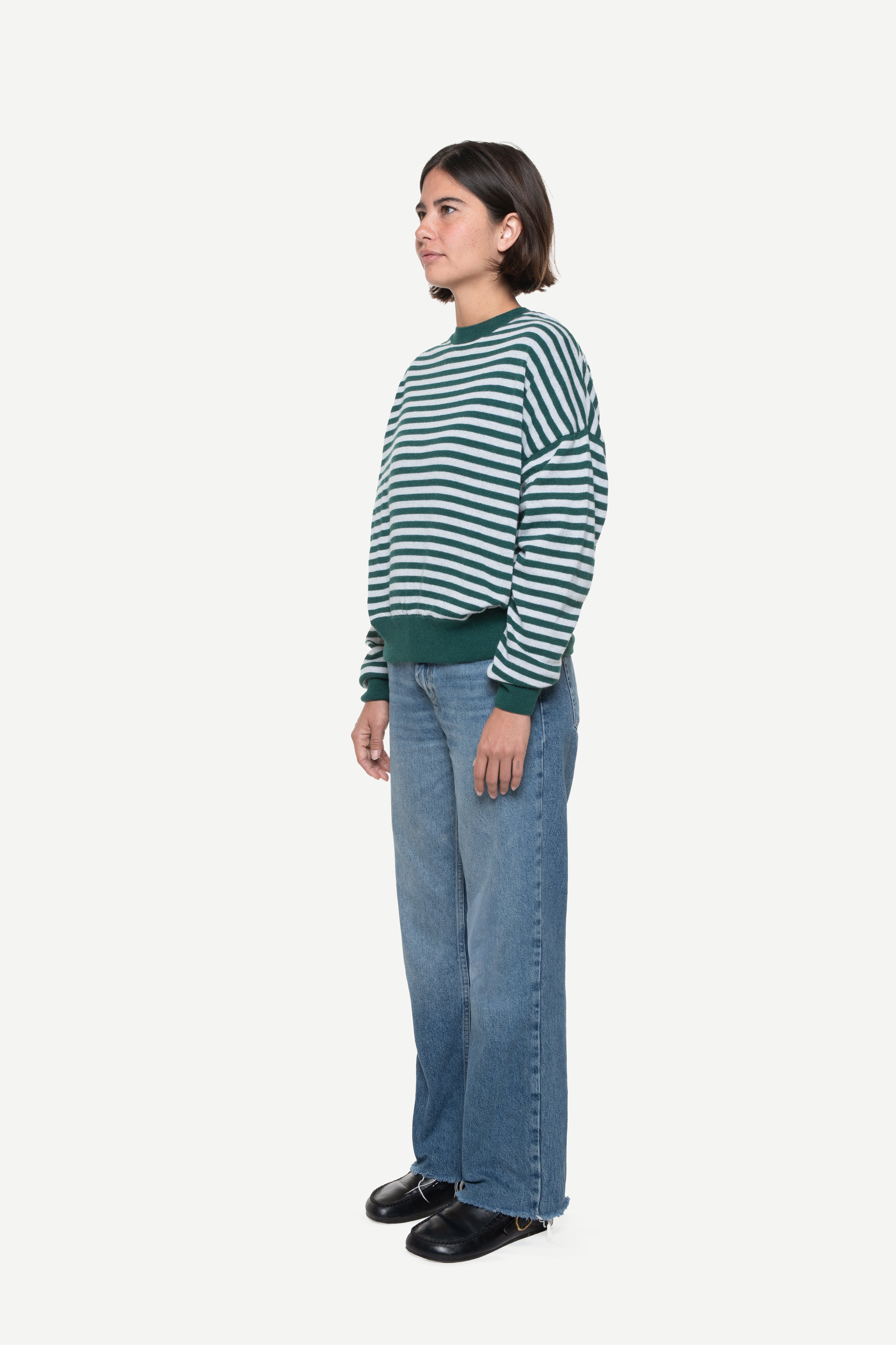 side view of a man wearing a blue knit striped sweater and jeans on a white background