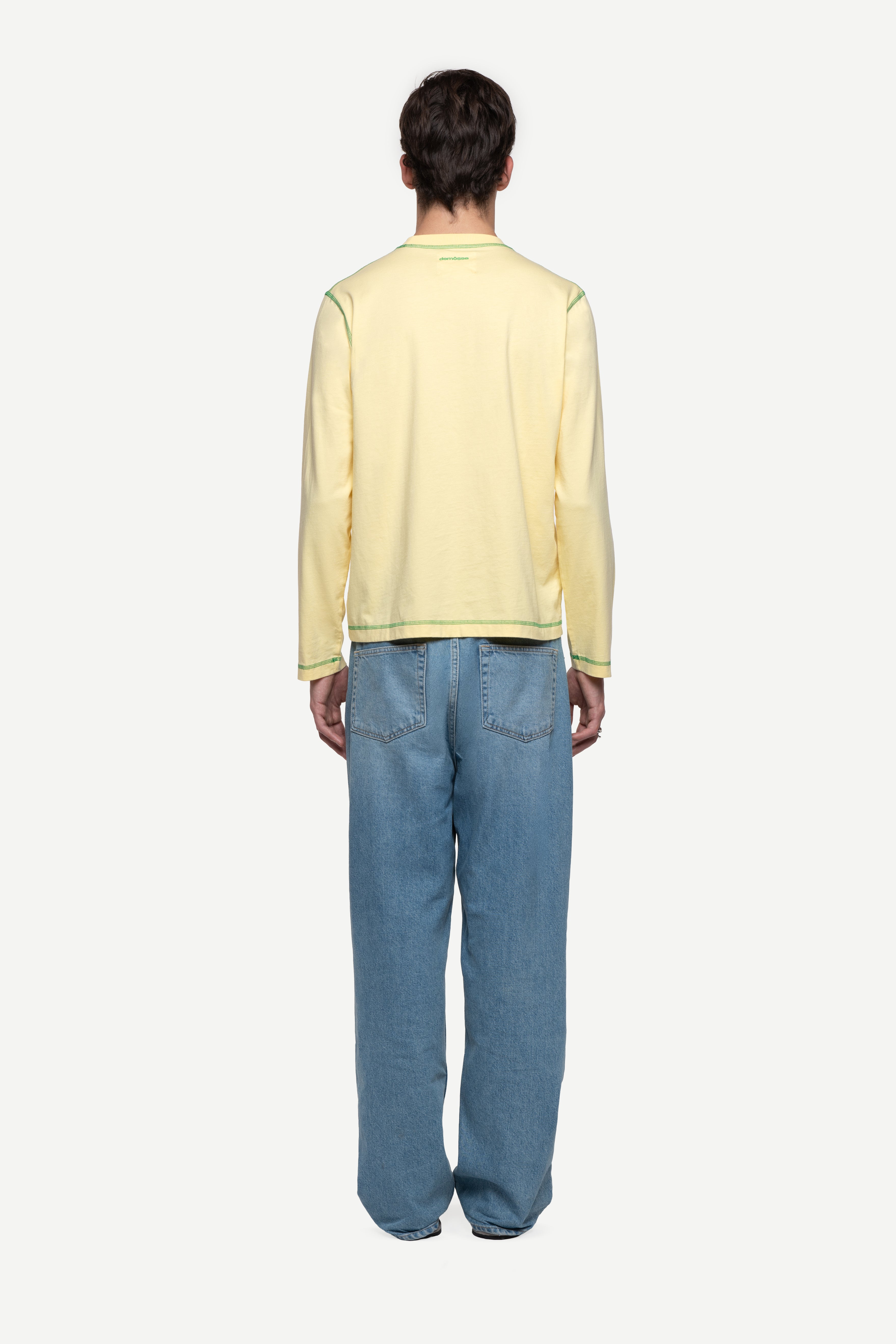 back view of man wearing a regular fit pale yellow red long-sleeved t-shirt with blue jeans and flip flops on a white background