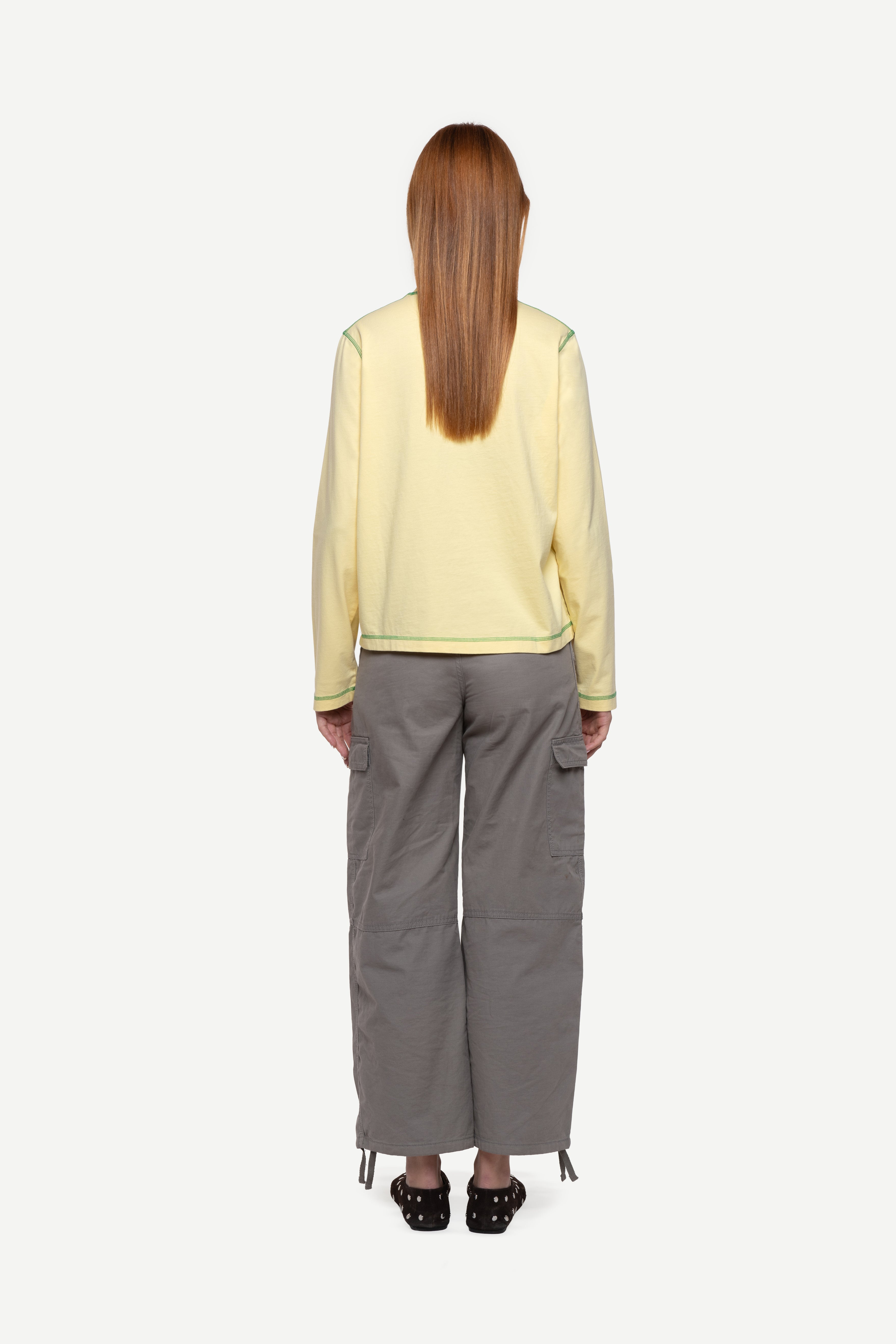 back view of woman wearing a regular fit pale yellow red long-sleeved t-shirt with cargo pants and ballet flats on a white background