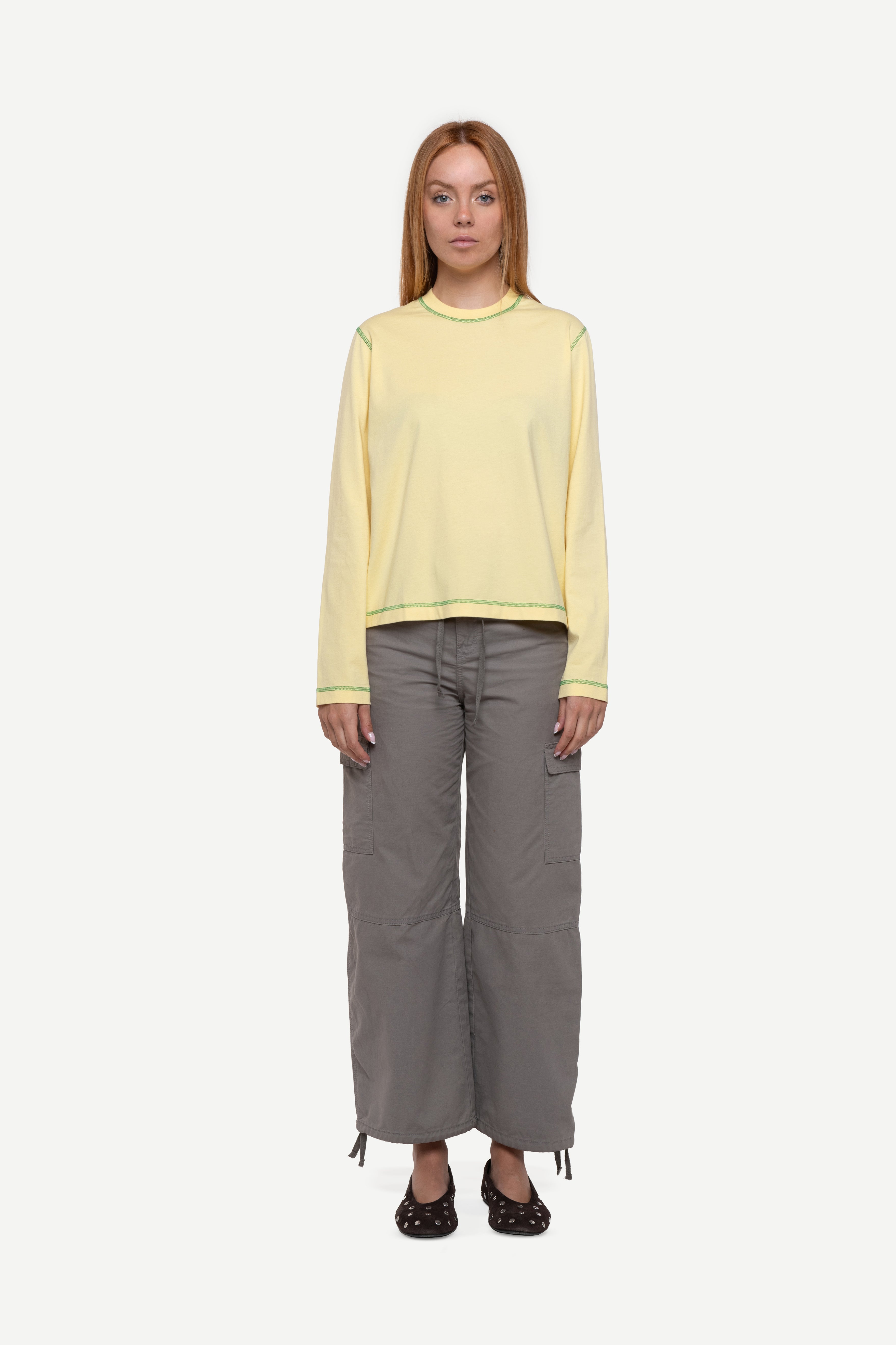 front view of woman wearing a regular fit pale yellow red long-sleeved t-shirt with contrast green over-lock stitching, cargo pants and ballet flats on a white background