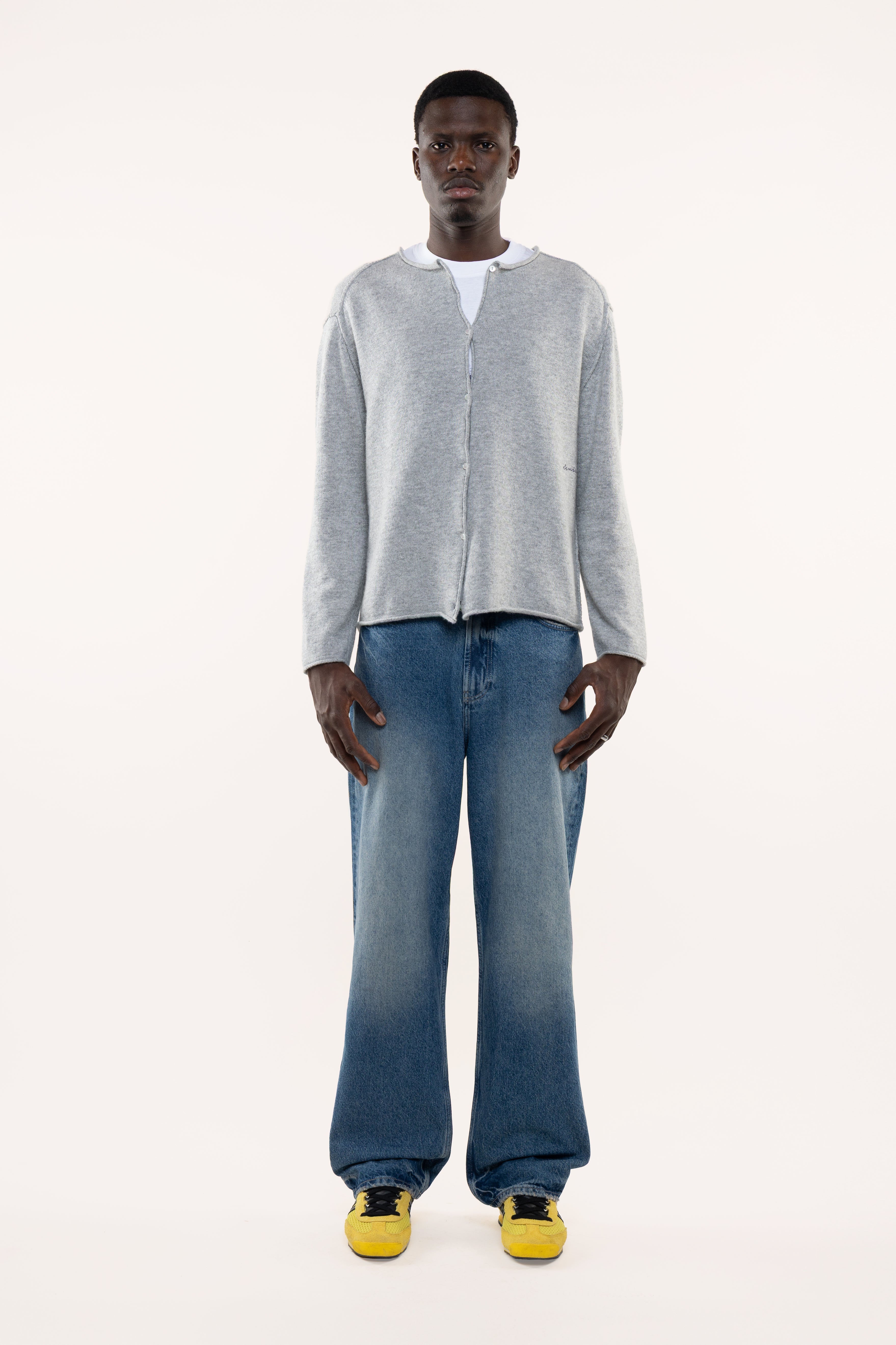 Man wearing a light gray buttoned cardigan and blue jeans on a white background