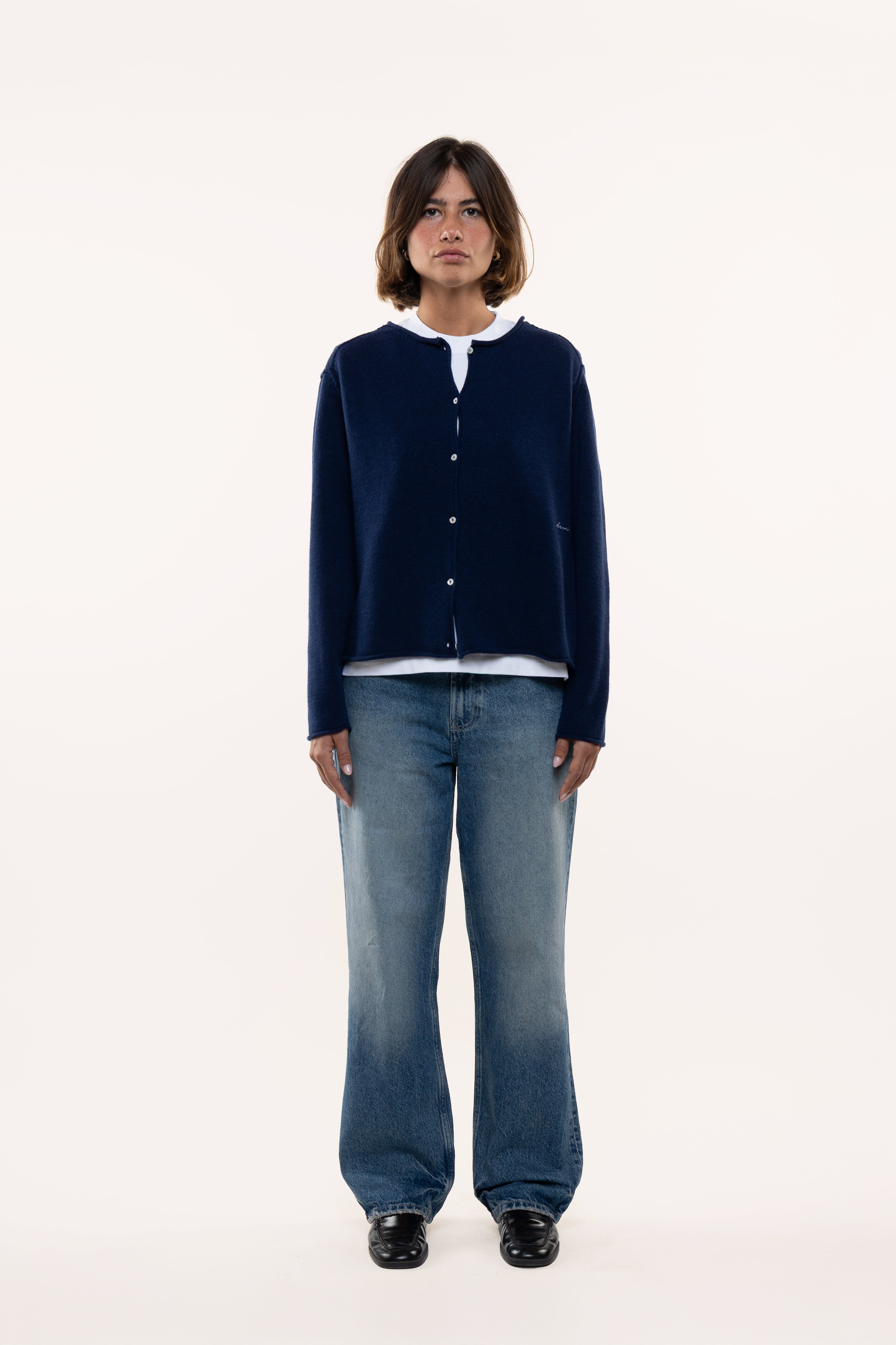 Woman wearing a navy cardigan, white shirt, and blue jeans on a white background