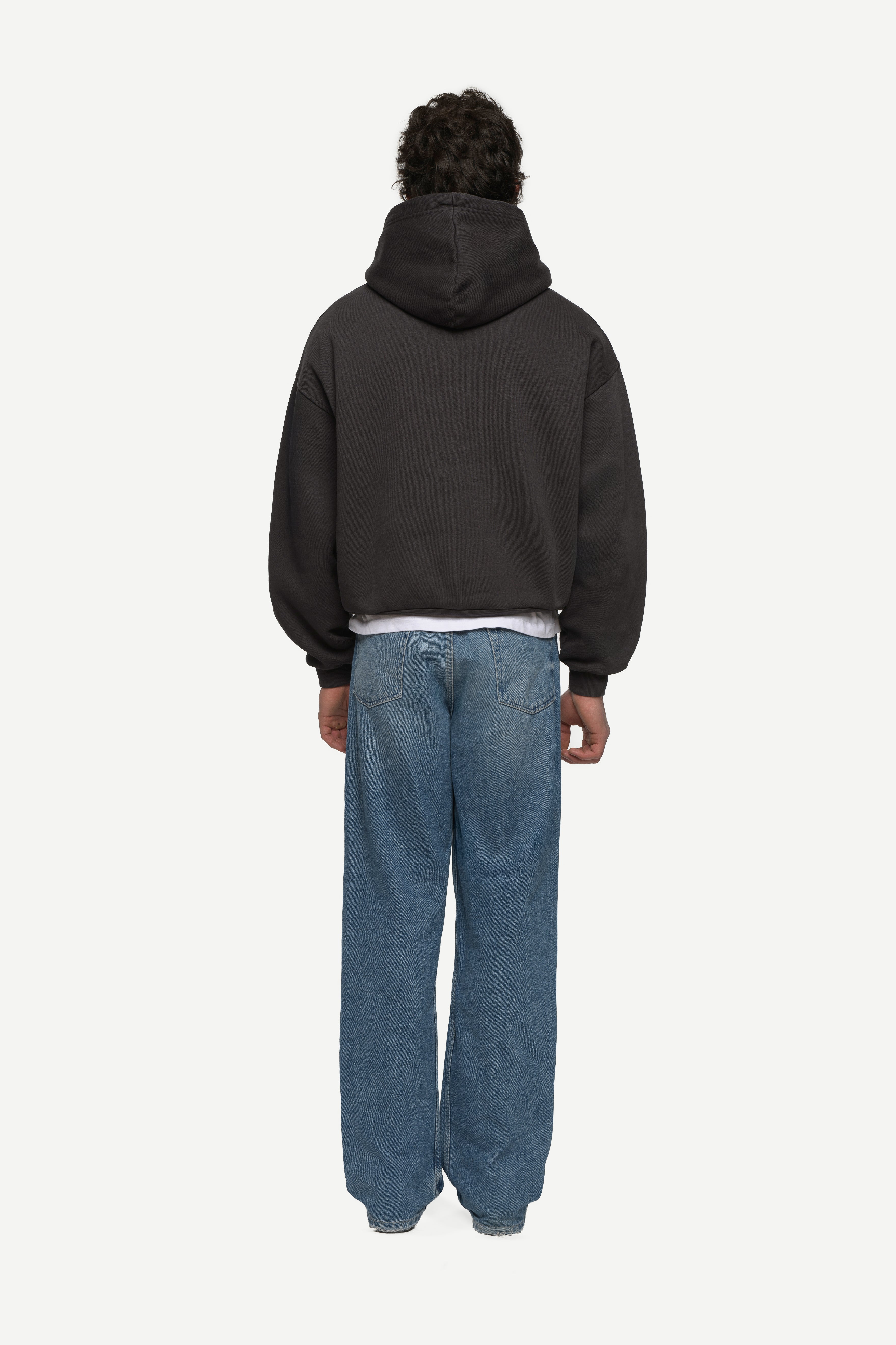 back view of man wearing a black hoodie and blue jeans on a white background