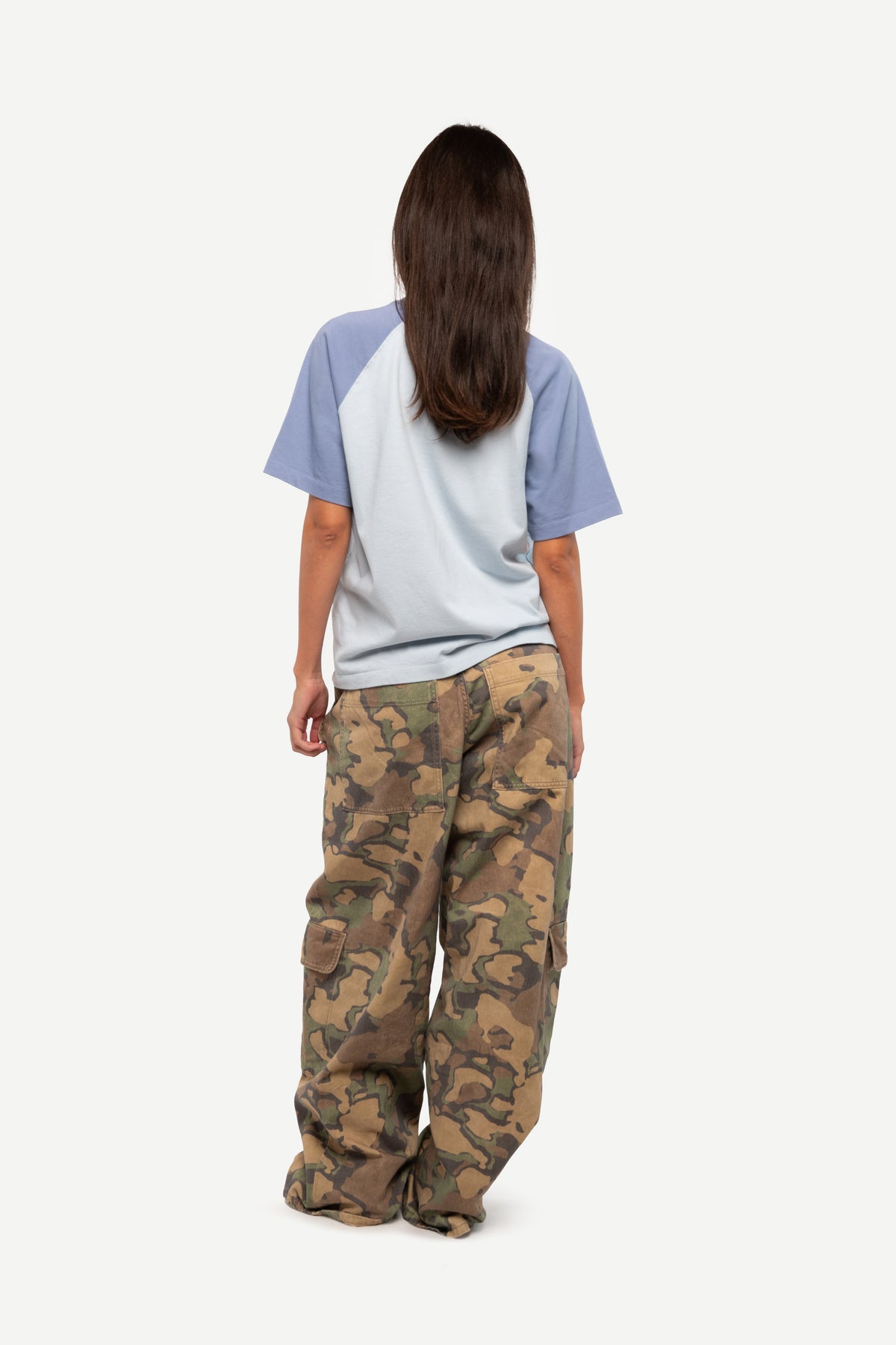 A child model shown from the back wearing a light blue and gray raglan t-shirt and loose-fit camouflage cargo pants, set against a plain light gray background.