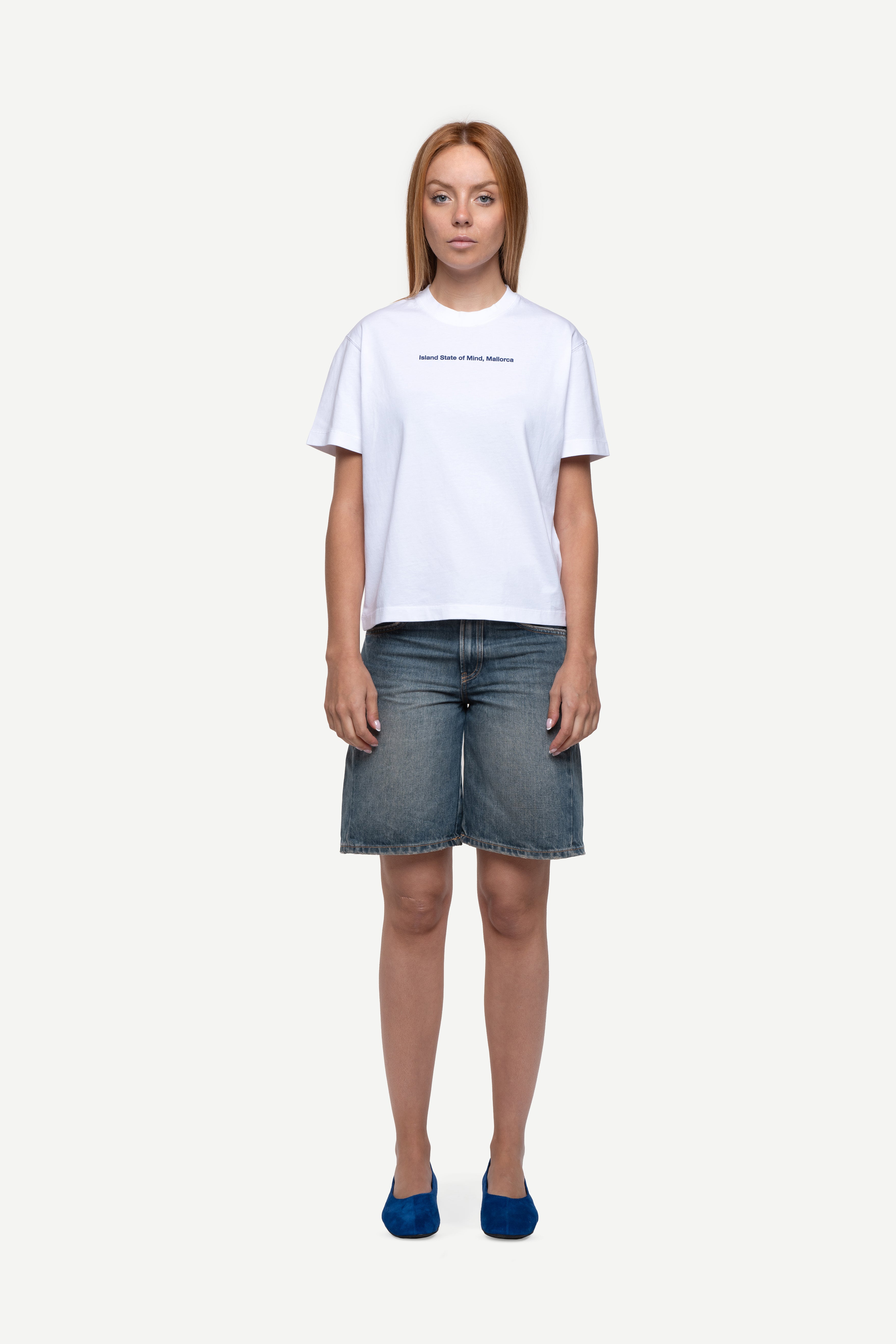 front view of woman wearing a regular fit black short-sleeved t-shirt with white double-layered neckline, sleeves and hem, blue jeans and flip flops on a white background