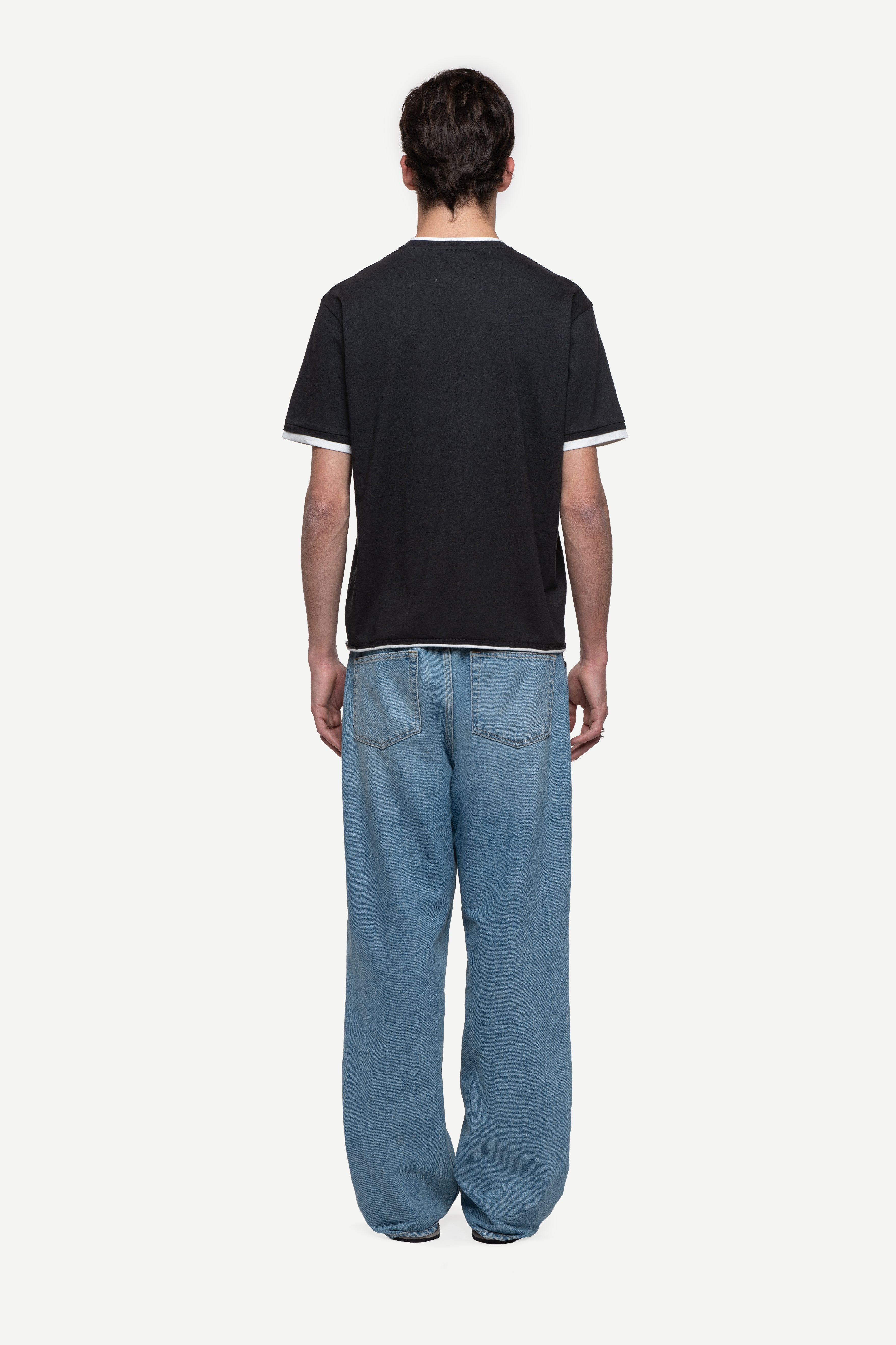 back view of man wearing a regular fit black short-sleeved t-shirt, blue jeans and flip flops on a white background