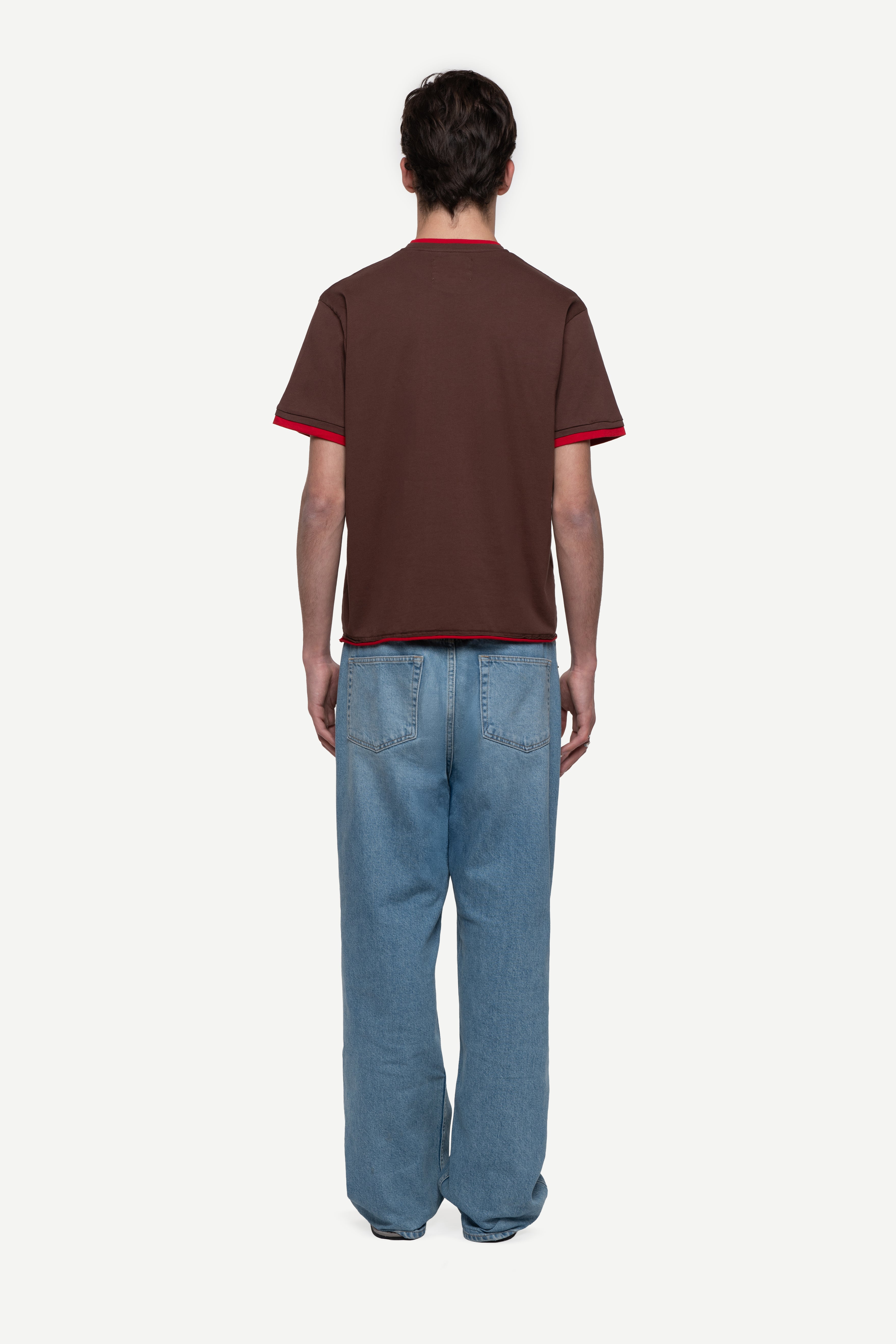 back view of man wearing a regular fit brown short-sleeved t-shirt, blue jeans and flip flops on a white background
